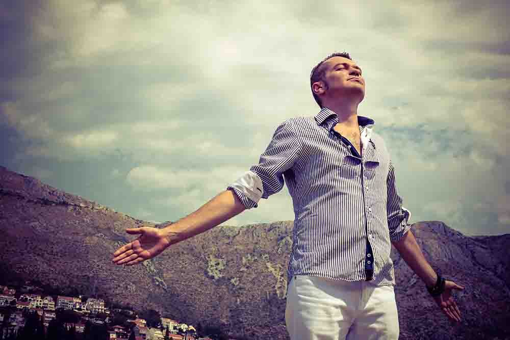 Carefree man enjoying in freedom with arms outstretched. Below view of man breathing fresh air with eyes closed.